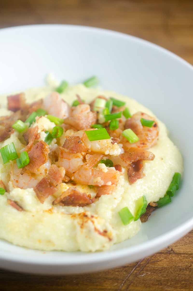 A bowl of creamy Shrimp and Grits topped with cooked shrimp, crispy bacon pieces, and chopped green onions.