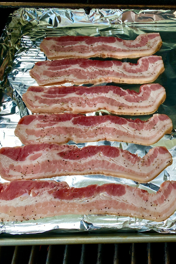 raw bacon with pepper on foil on cookie sheet raw meat on a foil pan