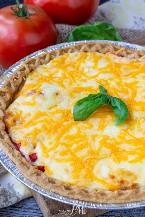 A classic Southern Tomato Pie topped with melted cheese and garnished with fresh basil, served in a foil pie dish, with ripe tomatoes and basil in the background.