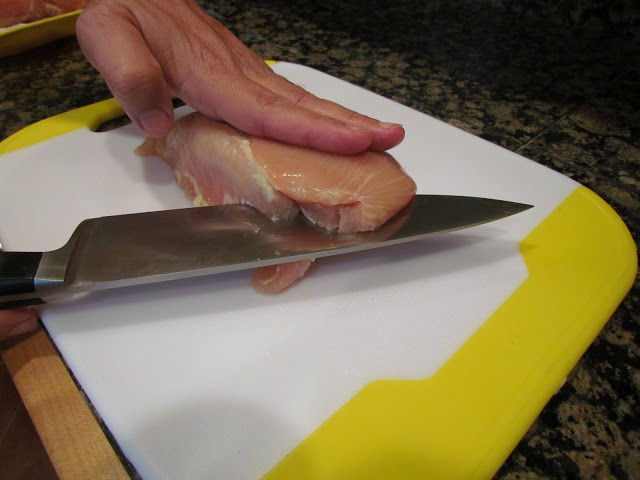 Using a sharp chef's knife to butterfly chicken breast on a cutting board.