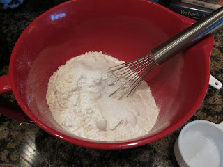 whisking baking ingredients in a red mixing bowl.