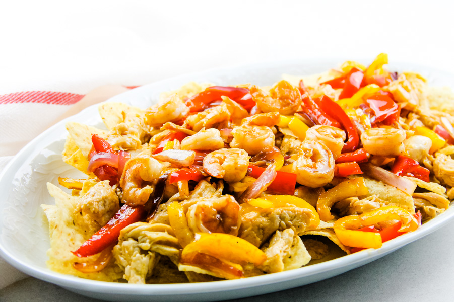 Chicken Shrimp Fajita Nachos are delicious when layered with all the good stuff chicken, shrimp, peppers, onions, and cheese. #chicken #shrimp #fajita #nachos White tray full of peppers and shrimp.