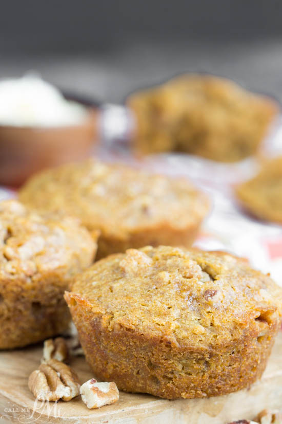Close-up of freshly baked pecan pie muffins with visible pieces of nuts, placed on a wooden surface with more muffins and a bowl in the blurred background.