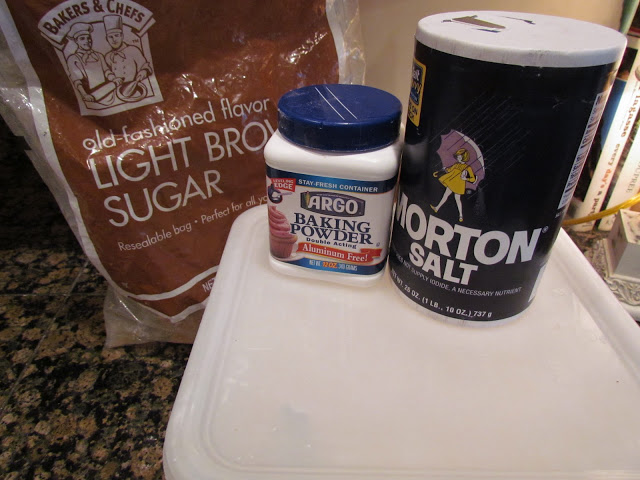 Containers of brown sugar, baking powder, and salt on a countertop.