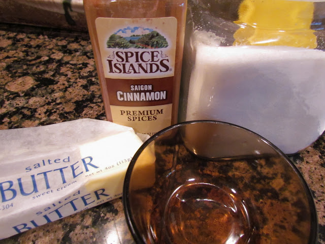 A stick of butter, white sugar, and ground cinnamon on a kitchen counter for a sweet biscuit recipe.