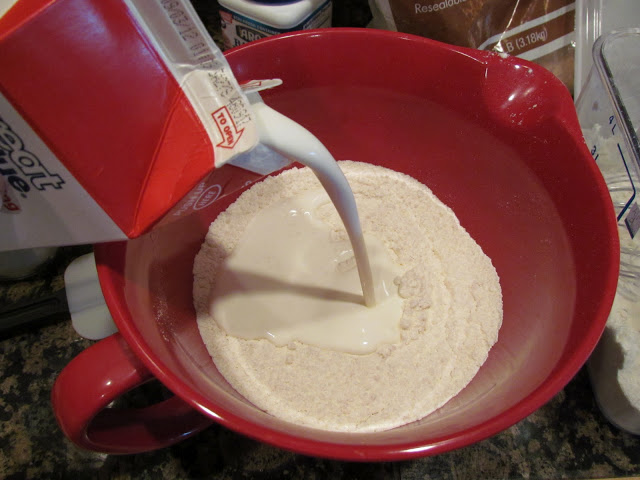 pouring heavy cream into a mixing bowl with flour.