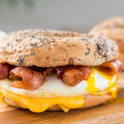 Bacon, egg and cheese breakfast sandwich with an everything bagel on cutting board