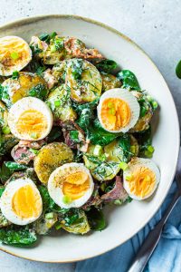 Traditional potato salad with bacon and eggs in a white bowl. Picnic food concept.