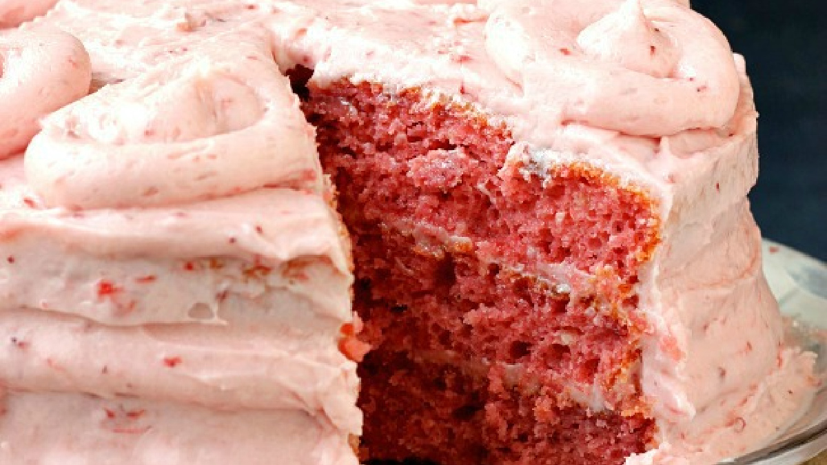 A pink frosted layer cake with a slice missing, showing its moist pink interior and thick, creamy strawberry frosting on top and between the layers—this Easy Strawberry Cake is as delightful to make as it is to enjoy.