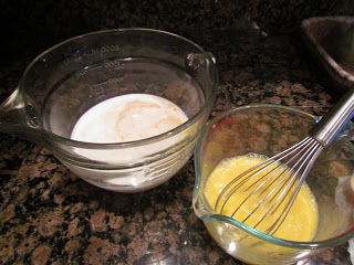 A bowl of milk and a bowl of eggs with a whisk.