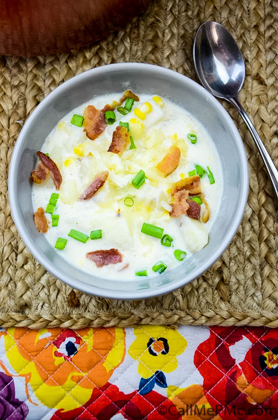 This deliciously creamy Corn and Potato Chowder is filled with diced potatoes, crispy bacon, and a sprinkle of green onion. It's comforting and coziness in a bowl! Bowl of creamy corn chowder with bacon on a woven placemat.