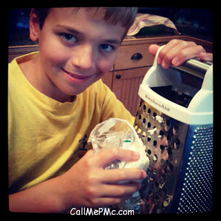 little boy grating cheese on a box grater.