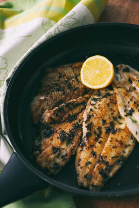 Pan Seared Catfish over Champagne Risotto with Champagne Pan Sauce has spicy seared catfish over a special champagne risotto is an elegant and flavorful special occasion dinner! #fish #catfish #champagne #risotto #sauce #recipe Cooked fillets with herbs in a black pan, garnished with a halved lemon.