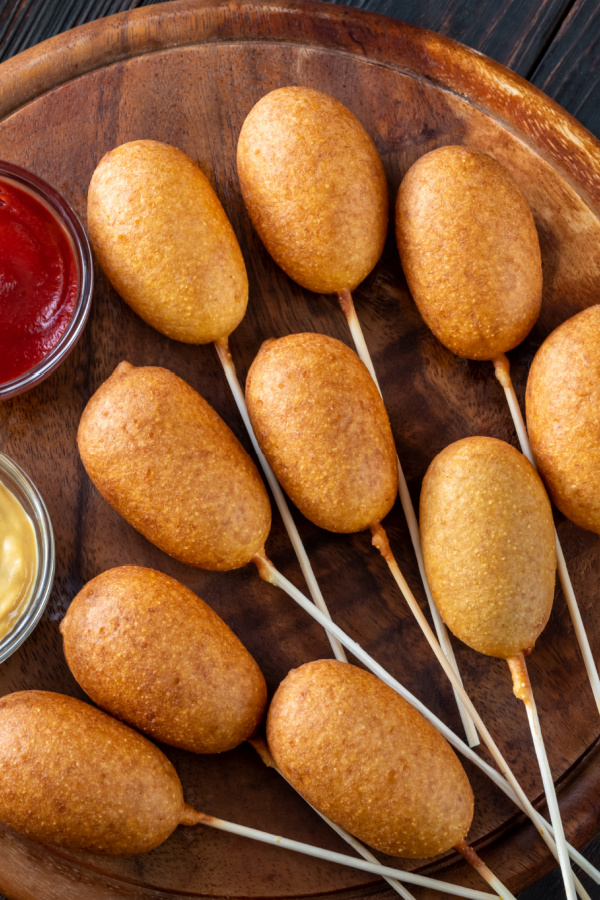 Corn dogs with different dip sauces on wooden board
