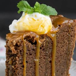 A slice of Irish Cream chocolate pound cake topped with whipped cream, caramel sauce, and a mint sprig graces the plate.