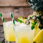 Fresh pineapple juice in two glasses with ice and mint leaves on dark rustic background