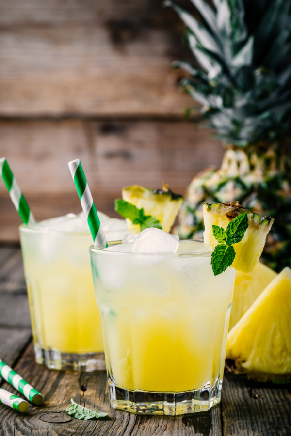 Tequila Pineapple Cocktail - Fresh pineapple juice in two glasses with ice and mint leaves on dark rustic background