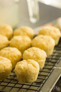 A batch of cheese muffins cooling on a wire rack, their golden tops reminiscent of freshly baked orange muffins, rests on a dark surface.