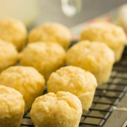 A batch of cheese muffins cooling on a wire rack, their golden tops reminiscent of freshly baked orange muffins, rests on a dark surface.