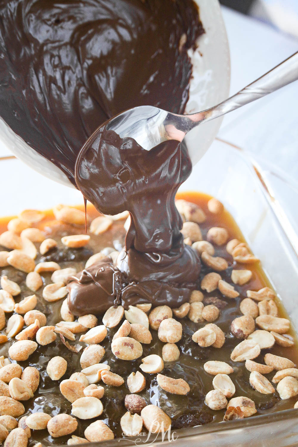 pouring melted chocolate over top of peanuts and nougat for copycat Snickers bars.