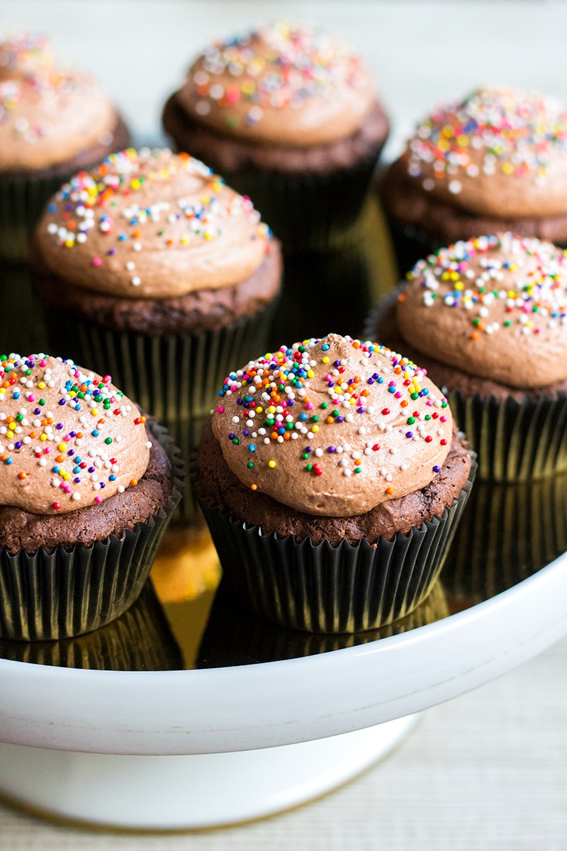 Chocolate Pudding Cupcakes Chocolate cupcakes with chocolate frosting and colorful sprinkles are arranged on a white cake stand, creating a tempting 50 Shades of Chocolate display.