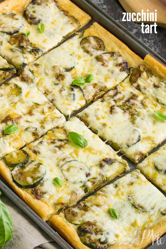 Fresh Zucchini Tart starts with an easy premade crust, topped with zucchini then smothered with cheese. #zucchini #baked A fresh zucchini tart, baked to perfection and cut into rectangular pieces, is topped with melted cheese and garnished with aromatic basil leaves.