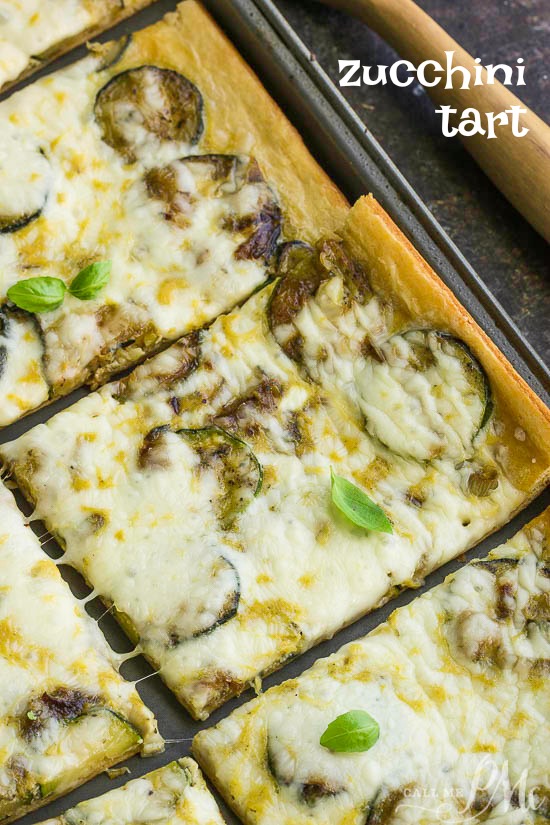 Fresh Zucchini Tart starts with an easy premade crust, topped with zucchini then smothered with cheese. #zucchini #baked A fresh zucchini tart, baked to perfection and cut into rectangular pieces, is topped with melted cheese and garnished with aromatic basil leaves.