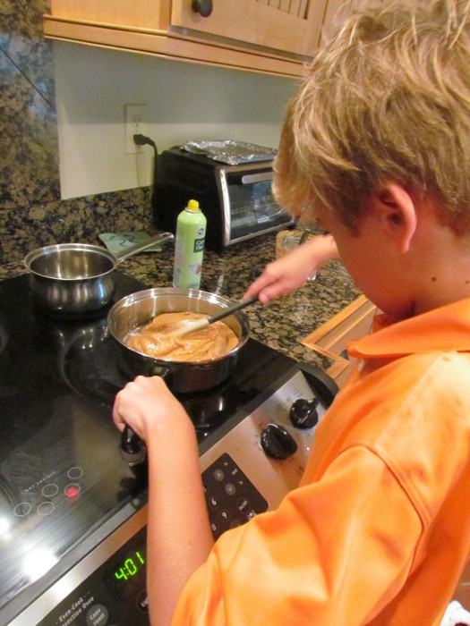 Young boy melting creamy peanut butter in a saucepan on the stove.