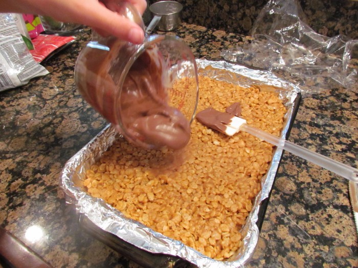 Pouring melted chocolate over crispy cereal treats.