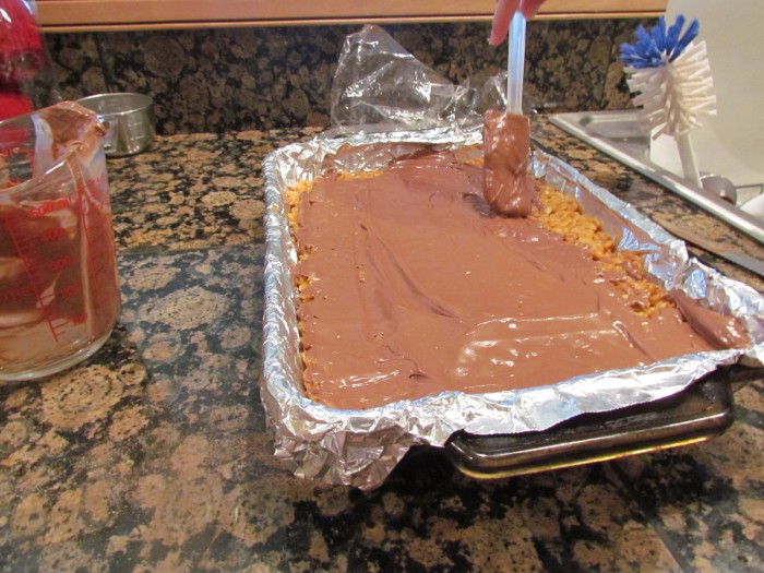 Spreading melted chocolate into a pan of peanut butter rice cereal bars.