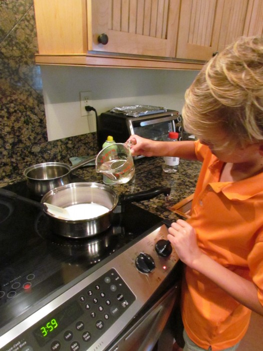 Young blonde haired boy combining water and sugar in a saucepan.