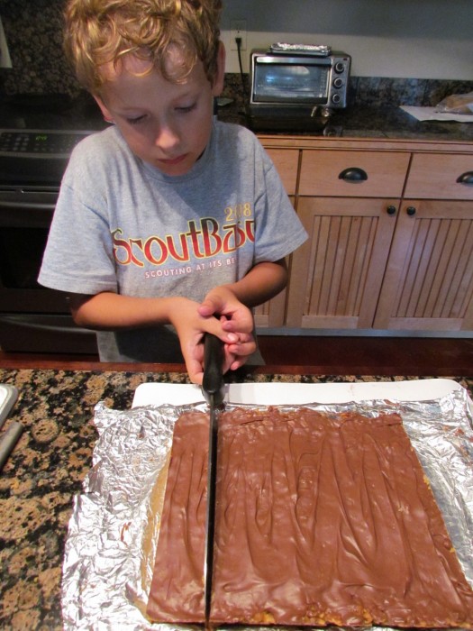 Young boy using a large knife to cut homemade peanut butter bars.