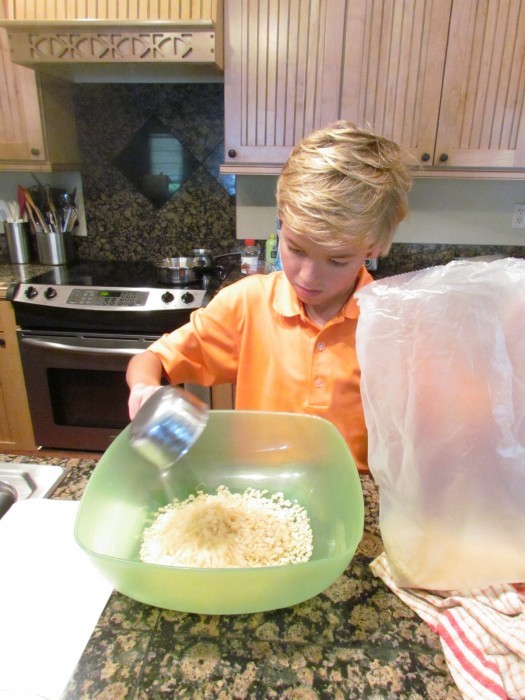 Blonde haired boy pouring Rice Krispies into a mixing bowl.