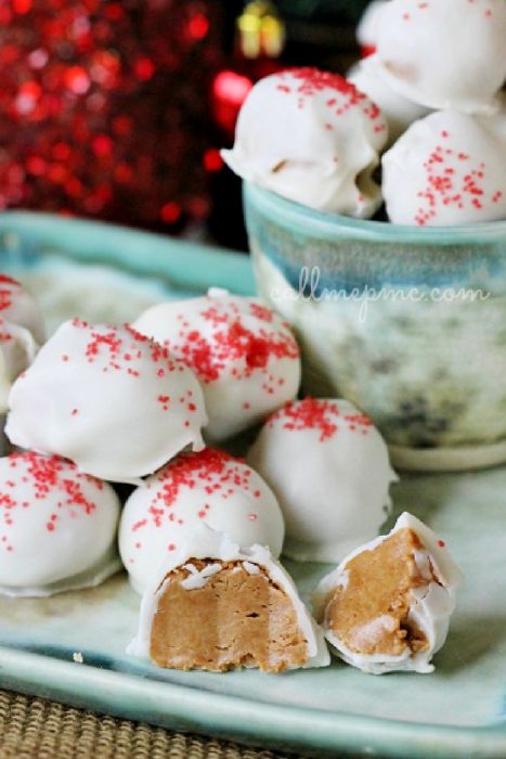 Three Ingredient Cookie Butter Truffles are literally what dreams are made of! Sweet and creamy cookie butter is elevated to superior status with the addition of confectioners' sugar and decadent white chocolate. #chocolate #cookiebutter #truffles #recipe #dessert #homemadegift White chocolate-coated Cookie Butter Truffle peanut butter balls topped with red sprinkles are arranged on a plate; one is cut open to reveal the creamy filling.