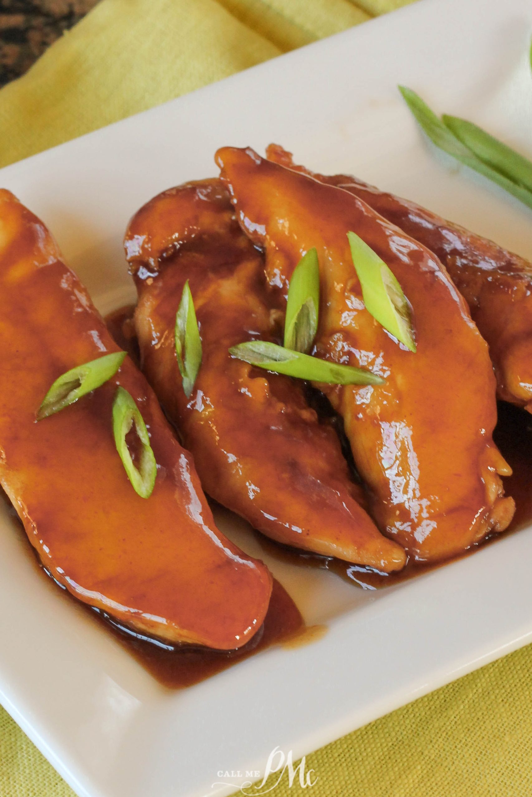 Three glazed chicken tenders, prepared using our Sticky Chicken Tenders Recipe, are topped with sliced green onions and served on a white rectangular plate.