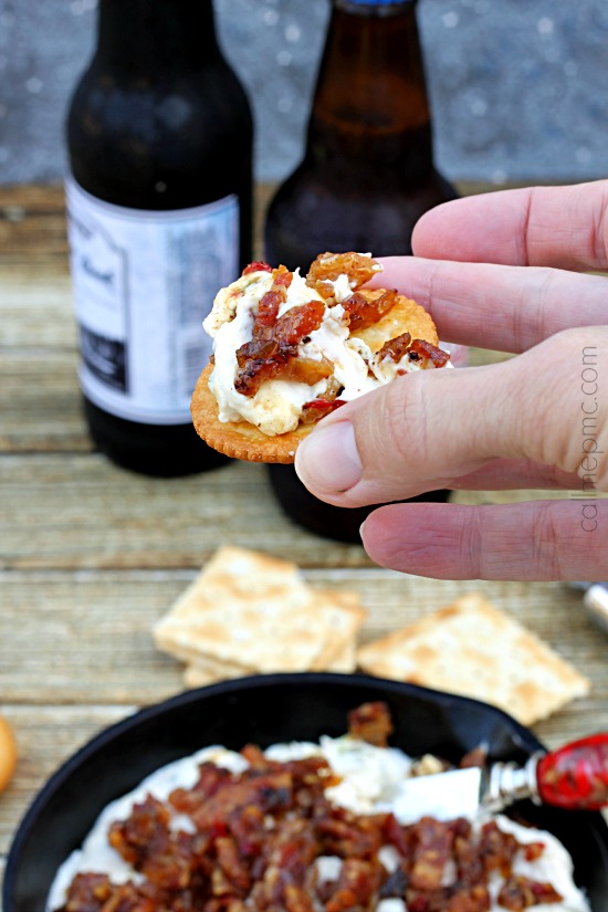 Salty, creamy and cheesy this Creamy Corn Bacon Dip is perfect for potluck, parties or tailgating. One bite of this flavorful sweet corn and crispy bacon and all your friends and family will be hooked! hand holding buttery cracker with creamy dip on it