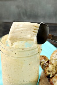 A spoon dives into a jar of creamy pepper sauce, reminiscent of a tangy white barbecue sauce, held just above the jar.