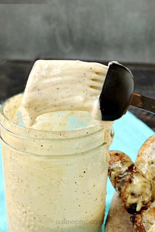 White BBQ Sauce for grilling barbecue chicken marinade dip A spoon dives into a jar of creamy pepper sauce, reminiscent of a tangy sauce, held just above the jar.