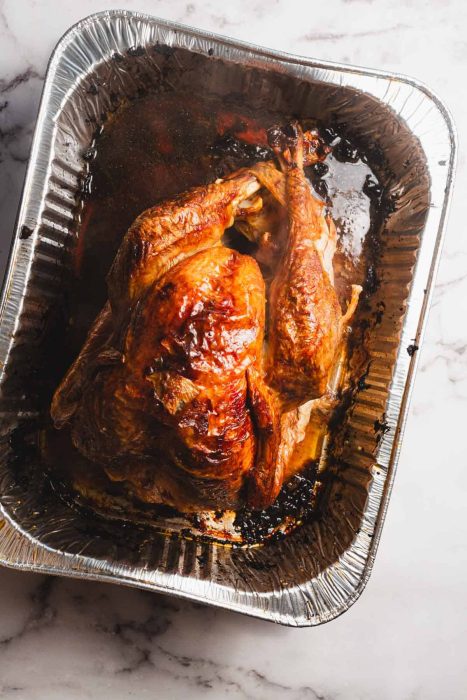 A roasted whole turkey, inspired by Best Turkey Recipes, sits in a disposable aluminum tray with browned, crispy skin and savory juices collected at the bottom.