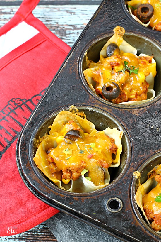 Sloppy Joe Wonton Cups Recipe A muffin tin is filled with baked taco cups topped with melted cheese and olives, sitting beside a red oven mitt, perfect for your next gathering.