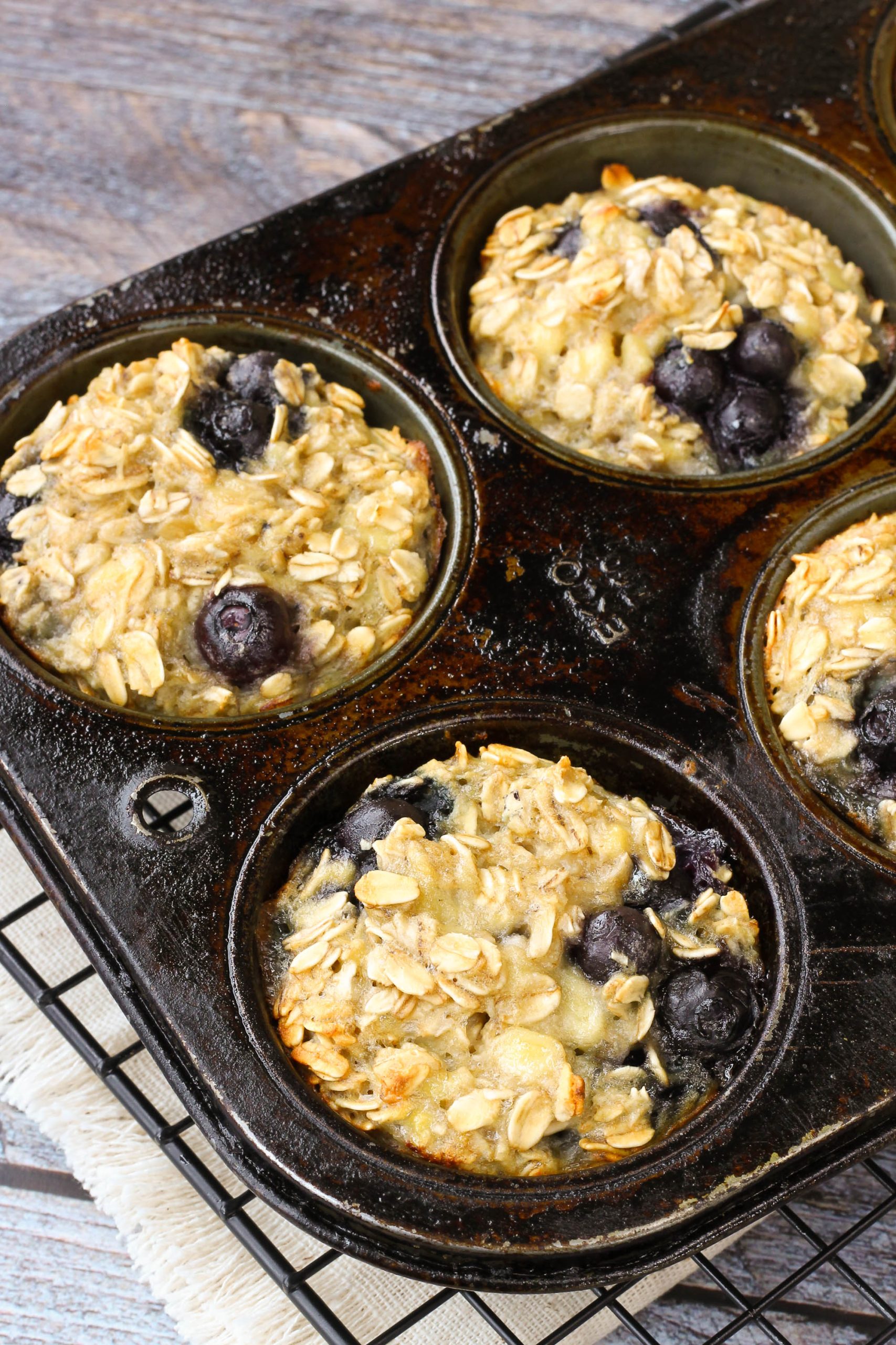 Healthy oatmeal blueberry muffins in muffin tin A muffin tin containing four Baked Blueberry Oatmeal Cups rests on a cooling rack, their golden tops studded with juicy berries.
