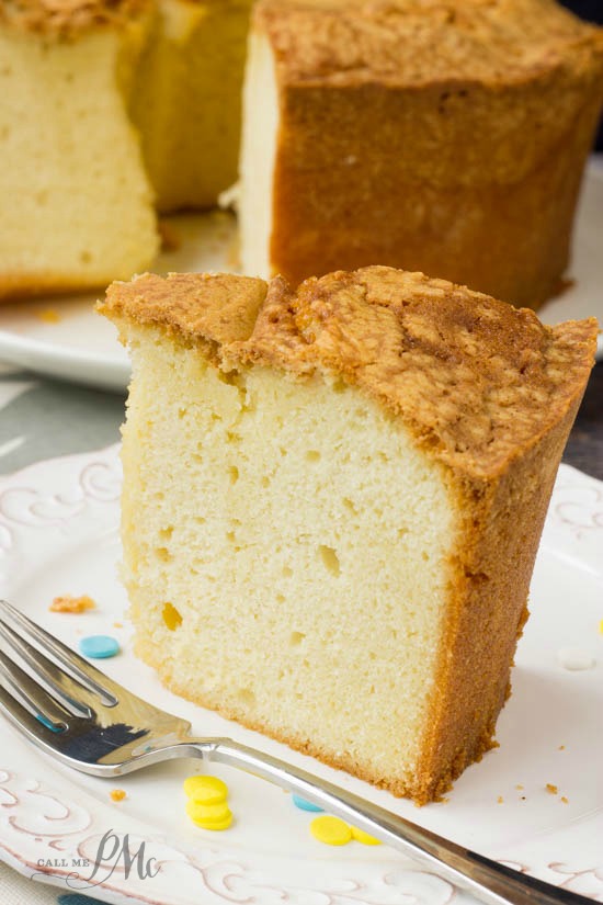A thick slice of Million Dollar Pound Cake sits on a white plate with a fork beside it; the rest of this decadent cake is visible in the background.