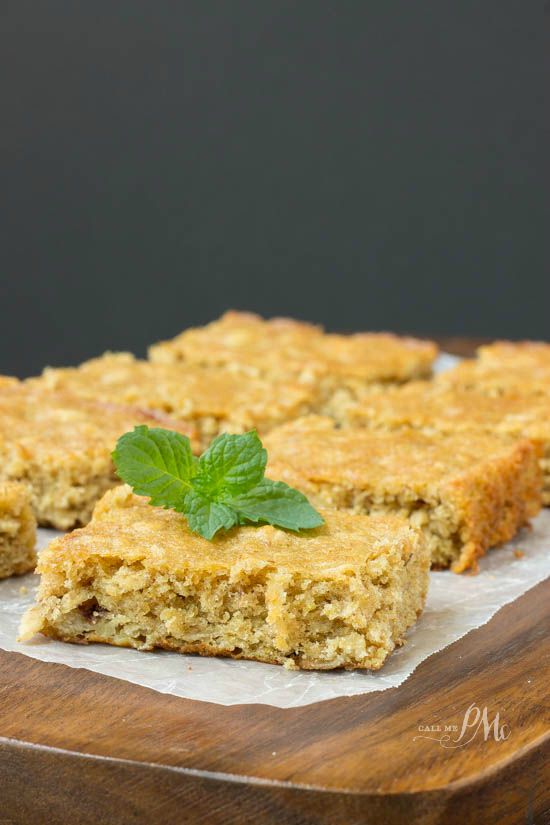 A close-up of freshly baked peanut butter oatmeal breakfast blondies garnished with a mint leaf on a wooden board.