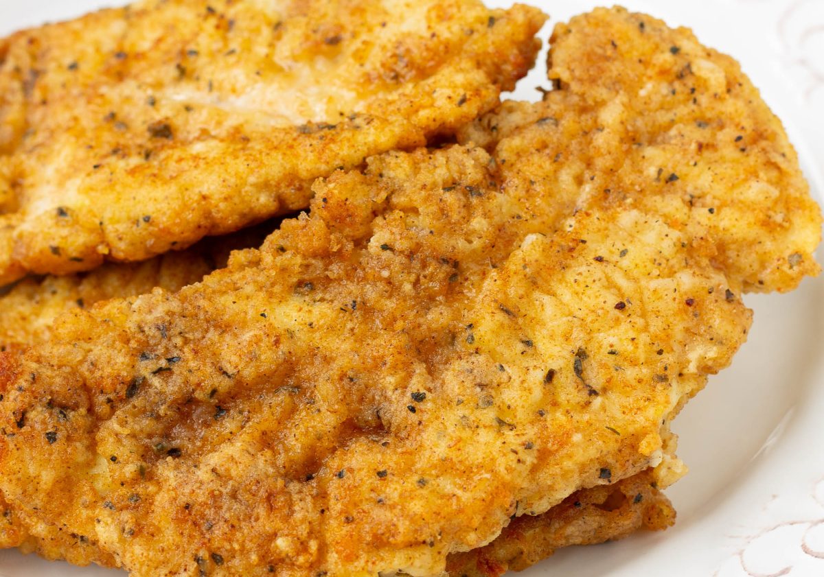 Close-up of several pieces of golden-brown, seasoned Copycat Chick-fil-a Chicken Strips on a white plate. crispy chicken strips recipe