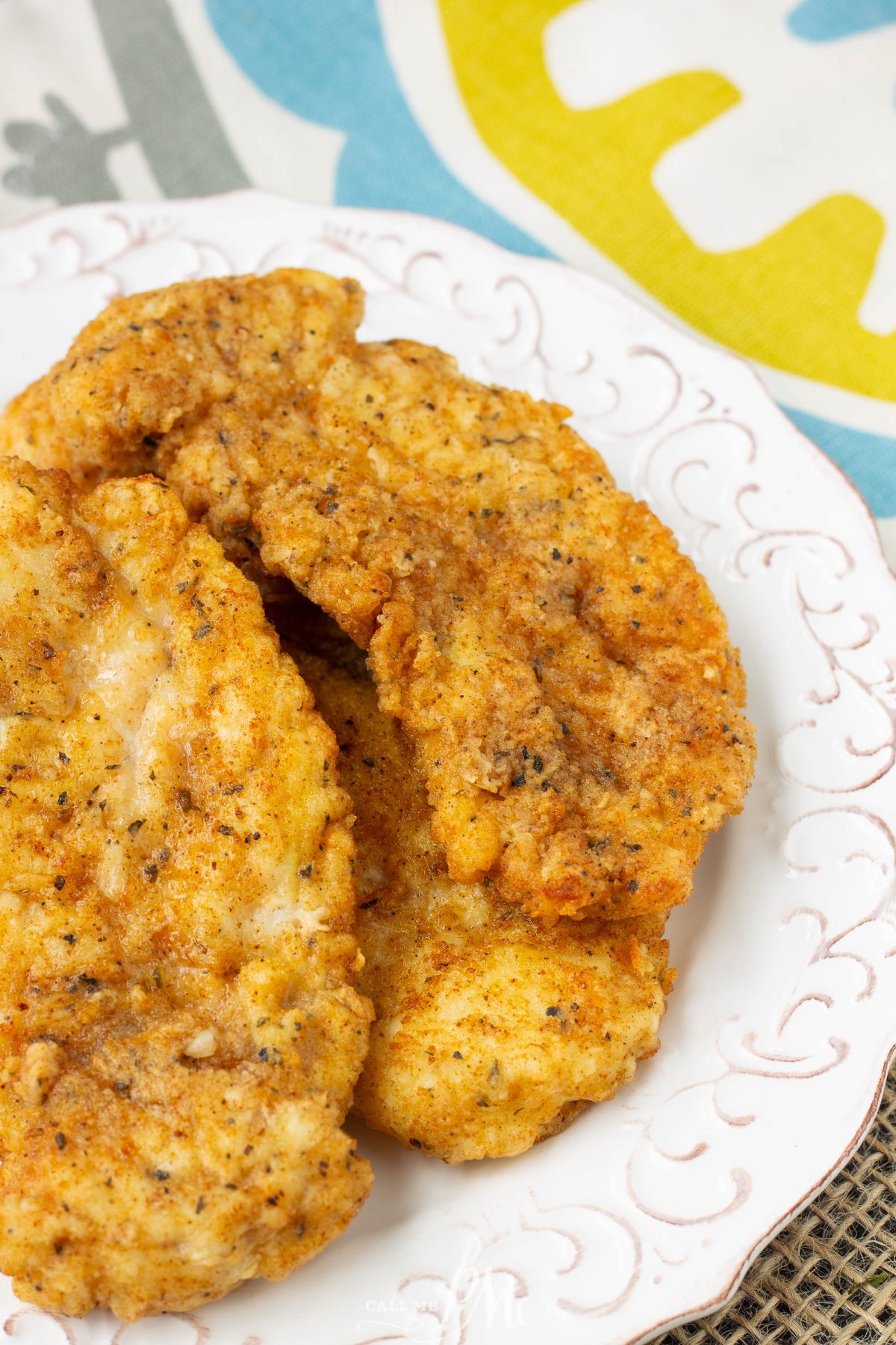 A plate with several pieces of golden-brown, seasoned copycat chicken tenders on a white patterned dish.