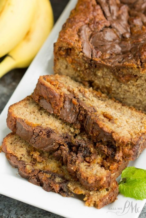 Three slices of Nutella Peanut Butter Banana Bread with a chocolate swirl are arranged on a white plate, with a loaf and bananas visible in the background.