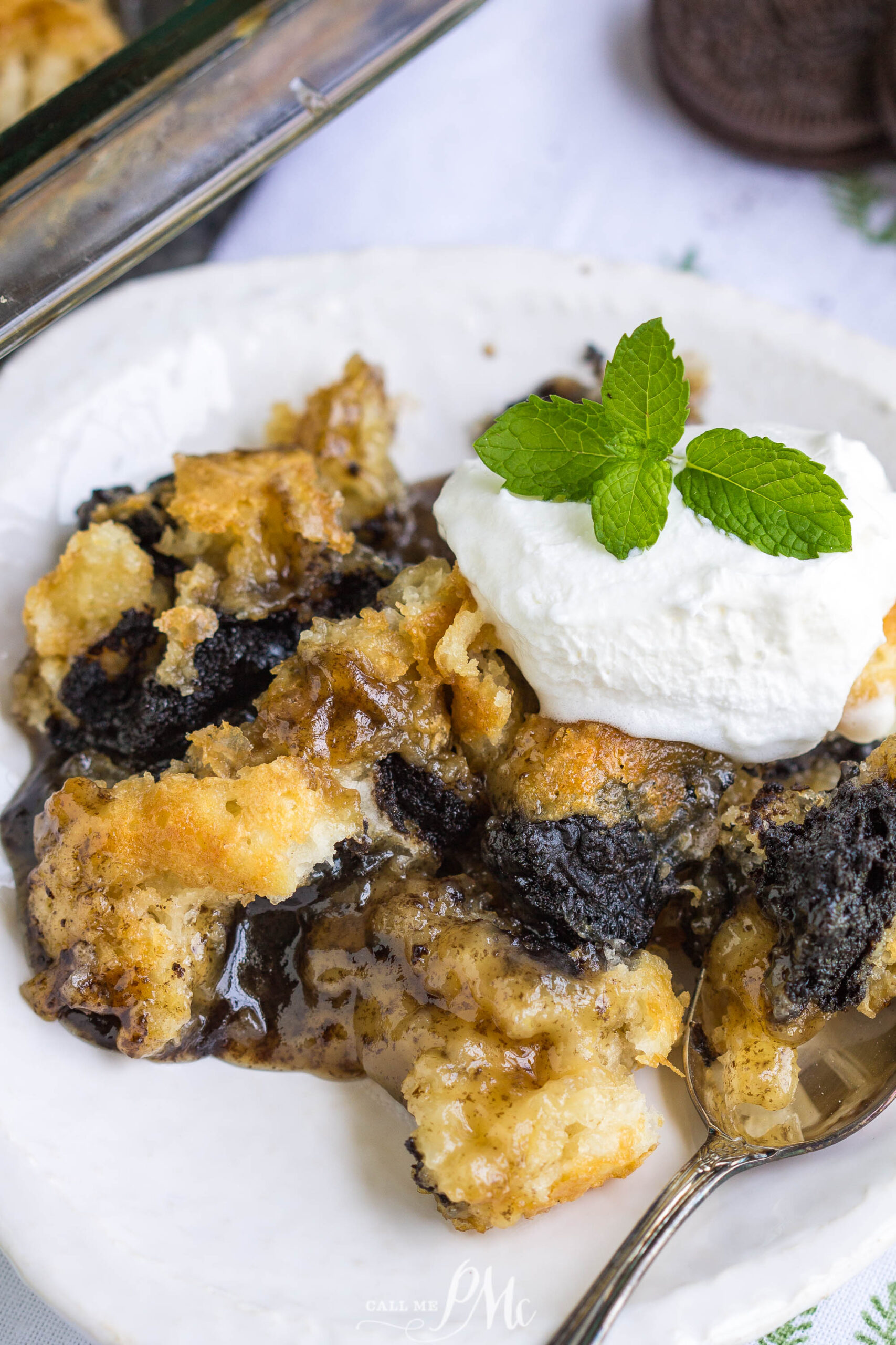 3 Step Oreo Cookie Dump Cobbler recipe. It's an easy dump-type dessert with crushed Oreo cookies A close-up of a dessert with whipped cream, and a sprig of mint on a white plate, with a spoon beside it.