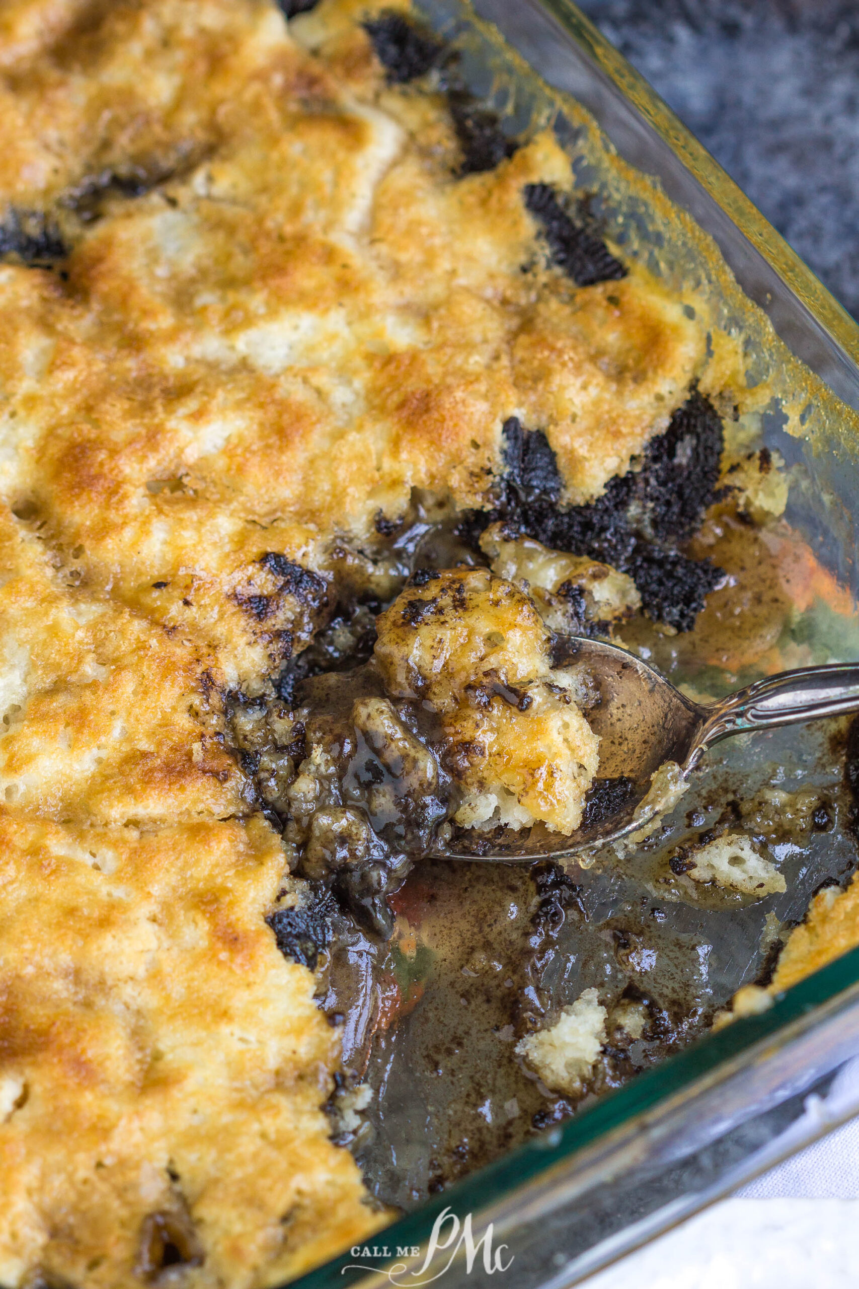 3 Step Oreo Cookie Dump Cobbler recipe. It's an easy dump-type dessert with crushed Oreo cookies A close-up of a dessert in a glass dish, with a spoon lifting a serving to reveal a dark, gooey filling under a golden, crumbly crust.