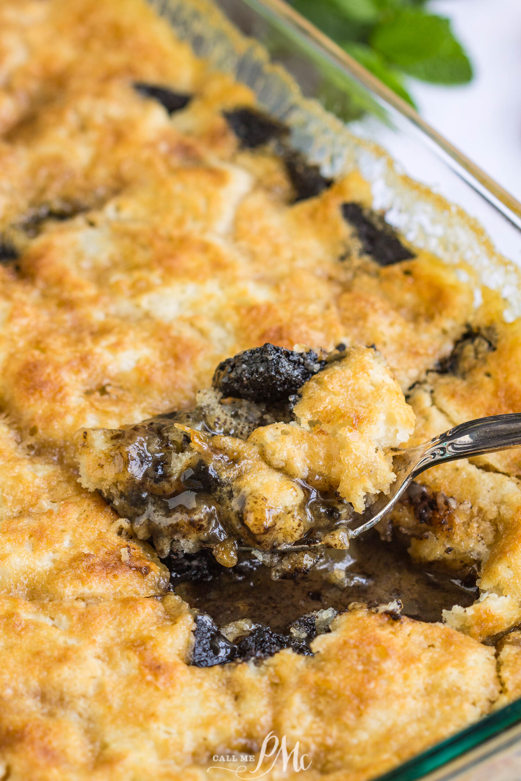 3 Step Oreo Cookie Dump Cobbler recipe. It's an easy dump-type dessert with crushed Oreo cookies A close-up of a 3 Step Oreo Cookie Dump Cobbler in a glass dish, with a spoon lifting a gooey, golden-brown portion to reveal a dark, syrupy filling studded with Oreo pieces underneath.