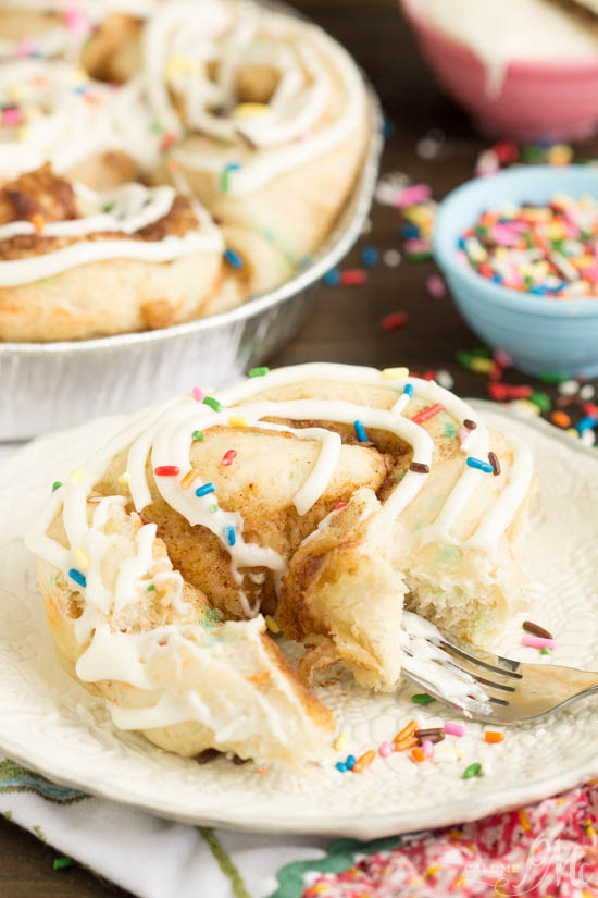 Tender and fluffy Birthday Cake Cinnamon Rolls is like having birthday cake for breakfast! #cinnamonrolls #cinnamon #bread #dough #yeast #birthday #celebration #recipe #breakfast iced cinnamon roll on white plate